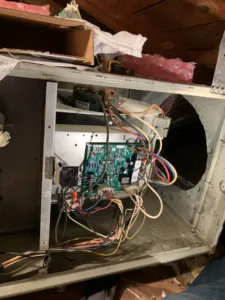 Certified Legit Air technician diagnosing and repairing a circuit board inside a modern furnace in a Fullerton, California home attic space.