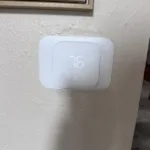 Legit Air Technician installing smart Thermostat upgrade and testing in Fullerton CA Home, you can see a newly installed Nest Brand white smart thermostat on a wall inside the residence