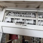 ac unit mounted on wall with coil being cleaned by foaming solution.